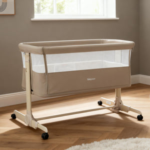 Beige babymore neera bedside crib with mesh sides and black caster wheels for easy mobility