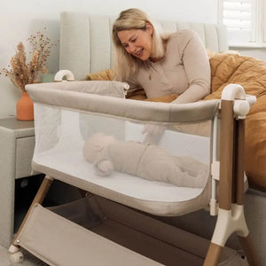 OBaby Cloud Bedside Crib Bundle Including Fitted Sheets – Oatmeal with baby and caregiver in a cozy setting.