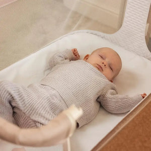 OBaby Cloud Bedside Crib Bundle Including Fitted Sheets – Oatmeal with a sleeping baby in cozy outfit.